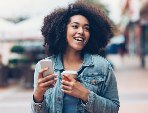 A young woman holding a smartphone and coffee cup